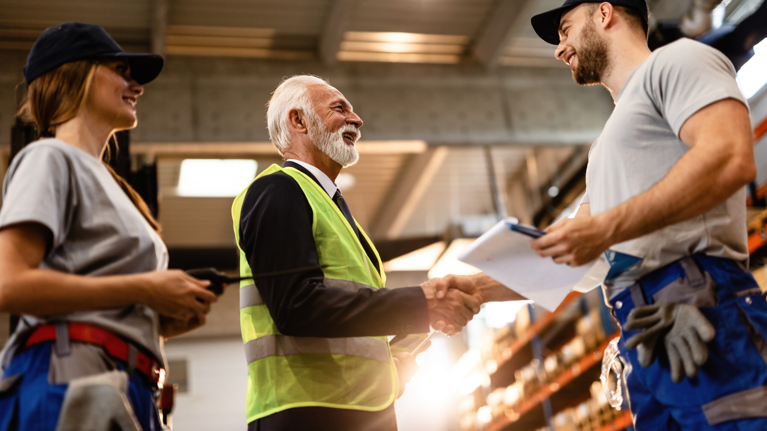 below view of happy mature businessman greeting workers in industrial building.